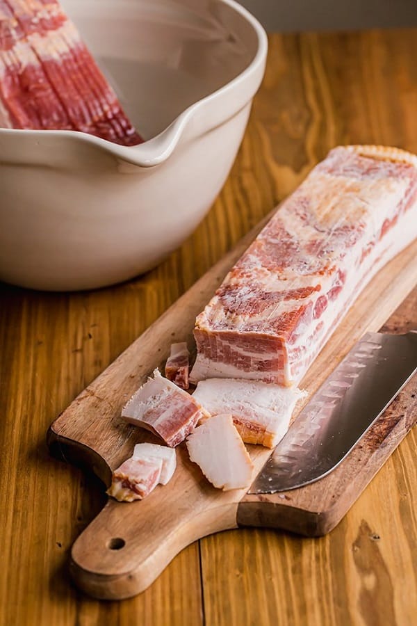 Slab of frozen bacon on a wooden cutting board with a large knife