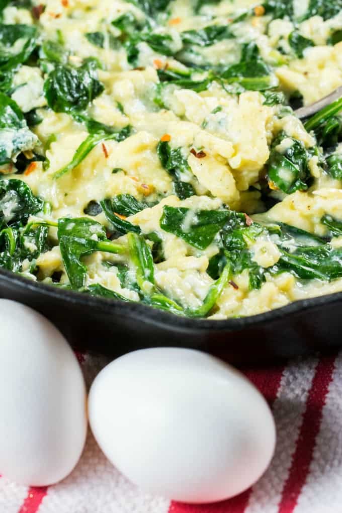 Close up of scrambled eggs with fresh eggs on the outside of the pan