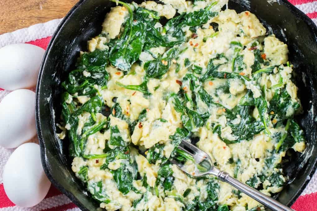 Cast iron pan with spinach and scrambled eggs with fresh eggs at the side