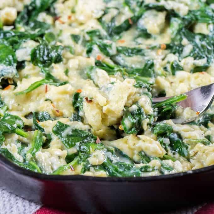 Cheesy Scrambled Eggs with Spinach in a cast iron pan with a fork