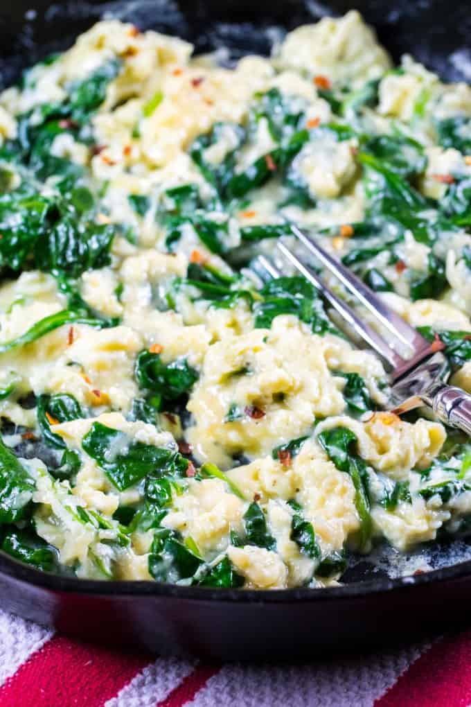Cheesy Scrambled Eggs with Spinach in a cast iron pan with a fork