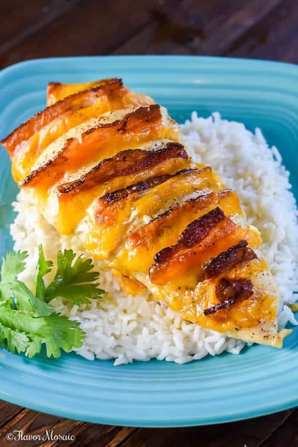 Hasselback chicken with bacon and cheese on a bed of rice on a blue dinner plate