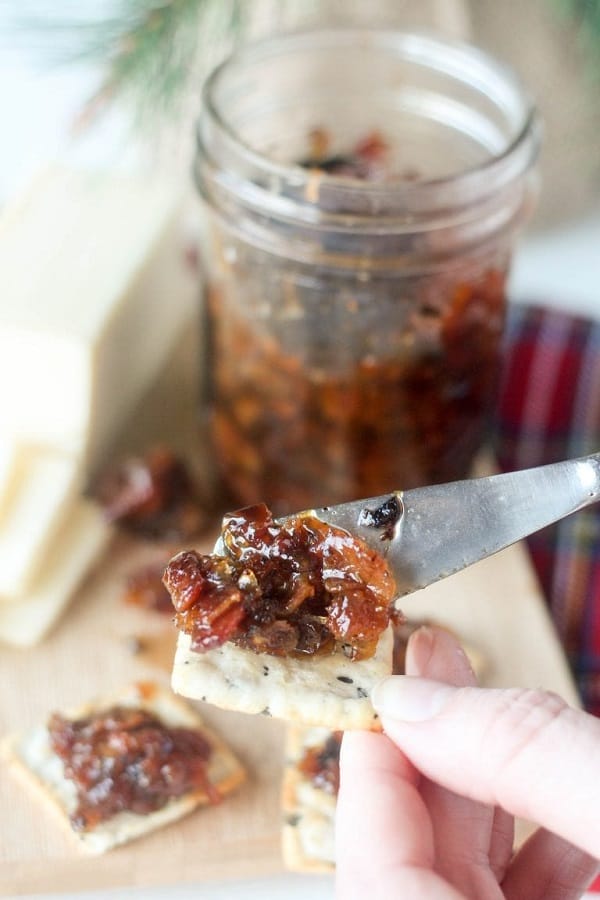 bacon jam on a knife with a cracker, the bacon jam jar is in the background