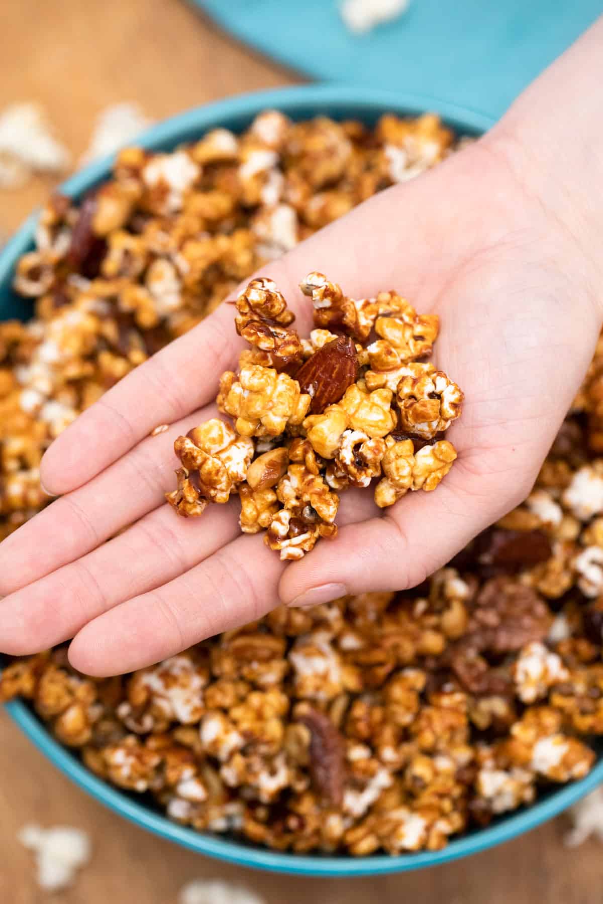 A Hand full of poppycock over a blue bowl full of poppycock