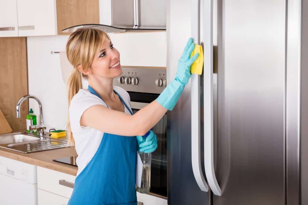Young Smiling Professional Cleaning Service Woman Cleaning Refrigerator In Kitchen