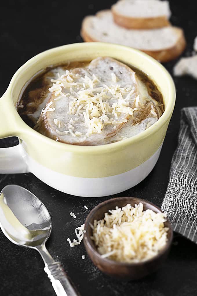 French onion soup in a bowl with a spoon and small bowl of Parmesan cheese