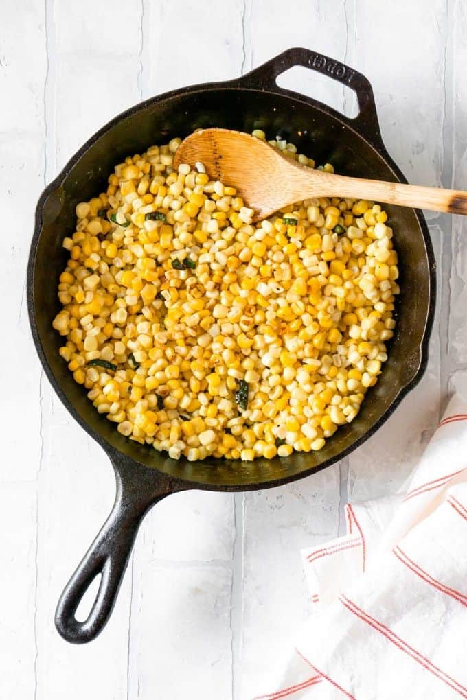 a cast iron skillet with corn and a wooden spoon