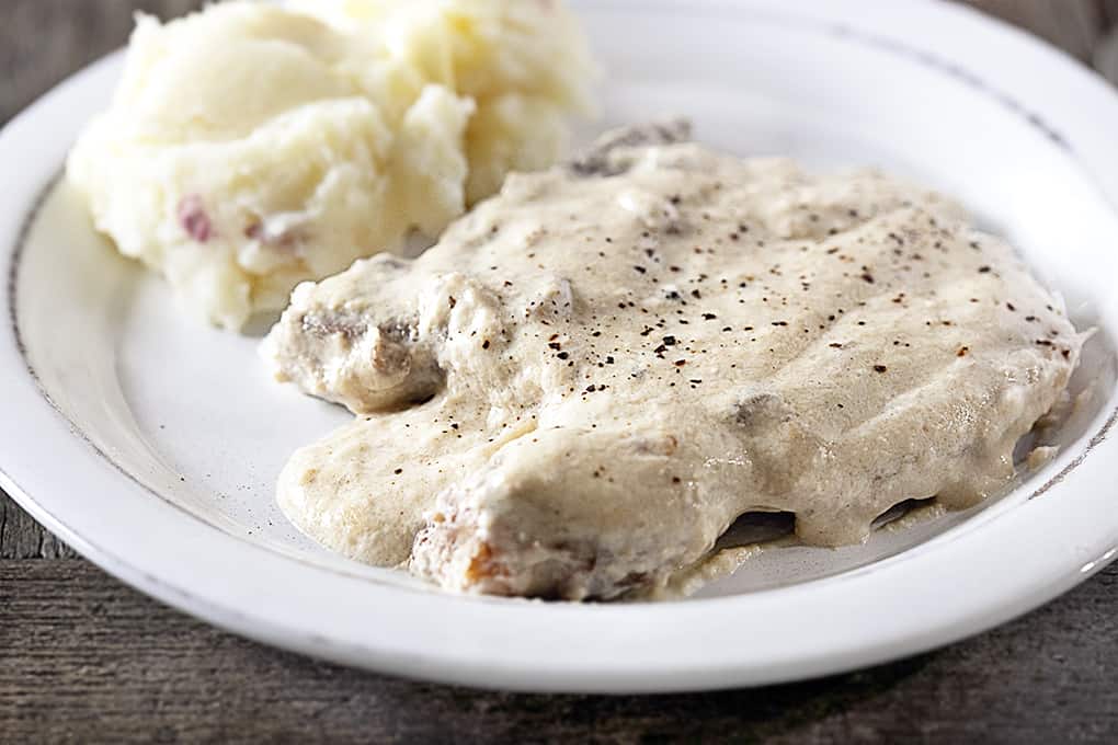 Slow Cooker Pork Chops on a white plate with mashed potatoes