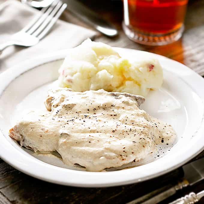 Pork chop in a cream sauce on a white plate with mashed potatoes