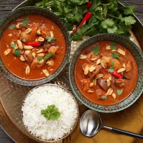 Peanut Butter Chicken Curry - A gold tray holds two bowls of bright brown curry, rice, cilantro and Thai red peppers.