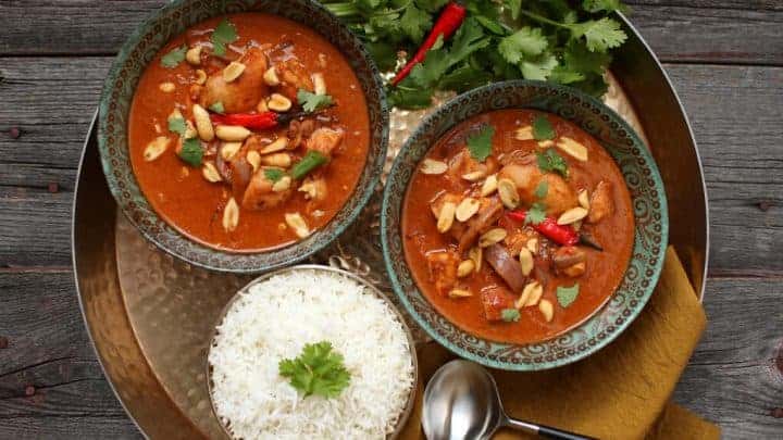 Peanut Butter Chicken Curry - A gold tray holds two bowls of bright brown curry, rice, cilantro and Thai red peppers.
