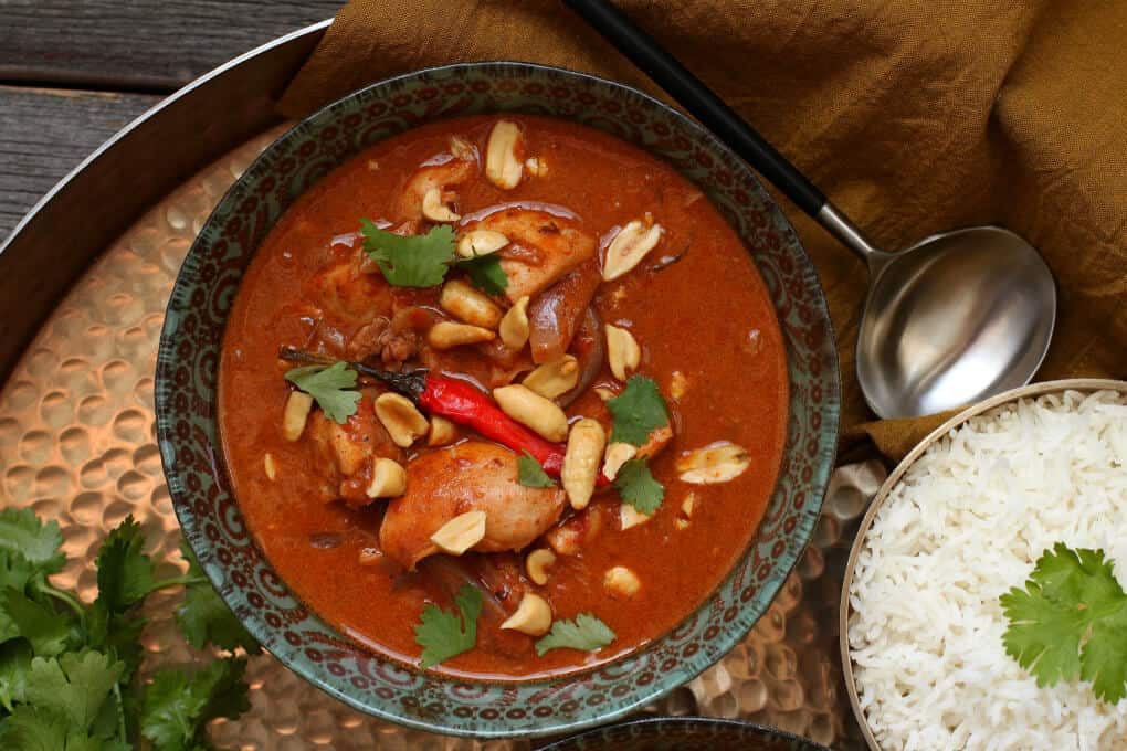 Peanut Butter Chicken Curry - close up of an ornate bowl filled with rich brown chicken curry topped with peanuts and cilantro.