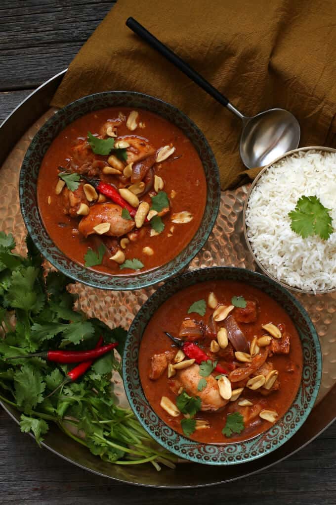 A gold tray holds two bowls of bright brown curry, rice, cilantro and Thai red peppers.