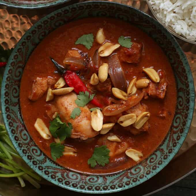 Close up of an ornate bowl filled with rich brown chicken curry topped with peanuts and cilantro.