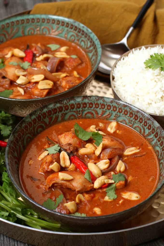 Peanut Butter Chicken Curry - A gold tray holds two bowls of bright brown curry, rice, cilantro and Thai red peppers.