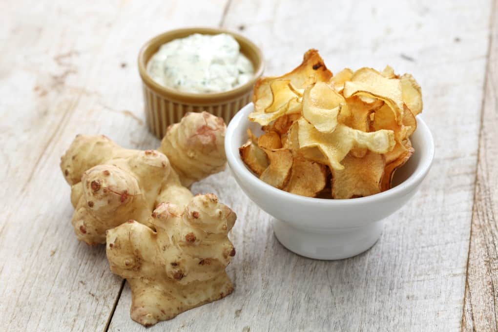 A sunchoke raw and a bowl of sunchoke chips with dip