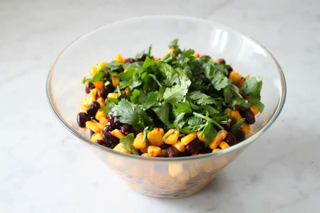 A glass bowl containing corn and beans topped with chopped cilantro. 