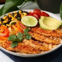 Healthy Chicken Burrito Bowl - A low white bowl filled with healthy vegetables, bean salad, avocado, rice, and chicken tenders.