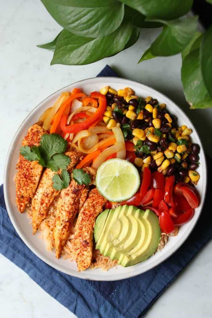 Healthy Chicken Burrito Bowl - overhead photo featuring a bowl filled with healthy vegetables, bean salad, avocado, rice, and chicken tenders. 