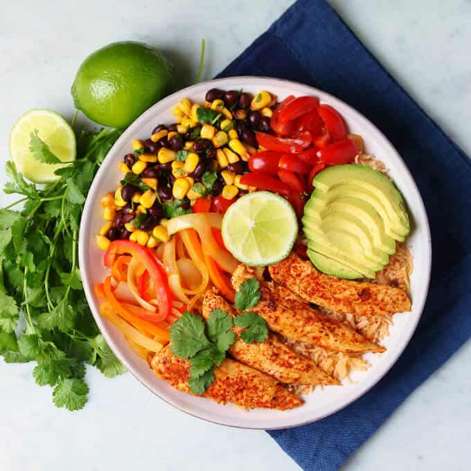 Healthy Chicken Burrito Bowl - overhead photo featuring a bowl filled with healthy vegetables, bean salad, avocado, rice, and chicken tenders. 