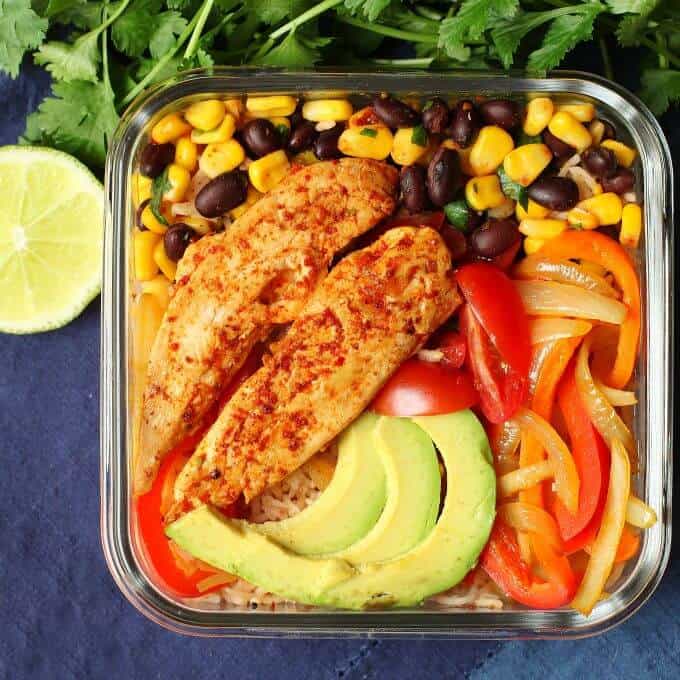 Healthy Chicken Burrito Bowl - overhead photo featuring a glass container filled with healthy vegetables, bean salad, avocado, rice, and chicken tenders. 