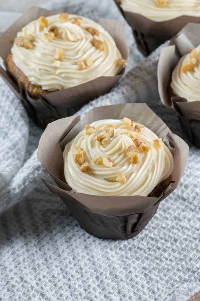 Carrot cake cupcakes with cream color frosting and walnut pieces in brown paper cupcake liners
