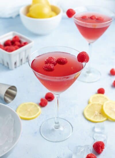 Chambord Bramble in a martini glass with lemon slices and raspberries around.