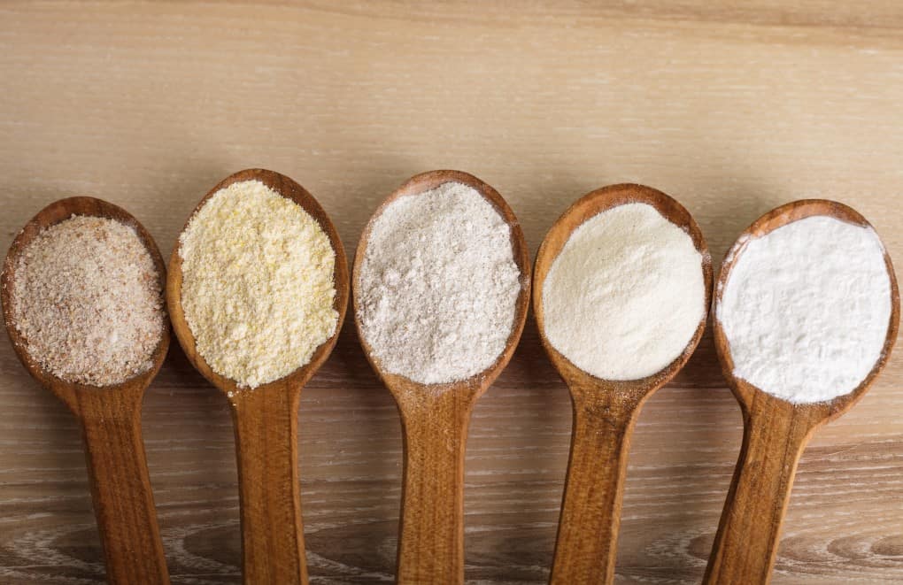 Various types of flour in five wooden spoons