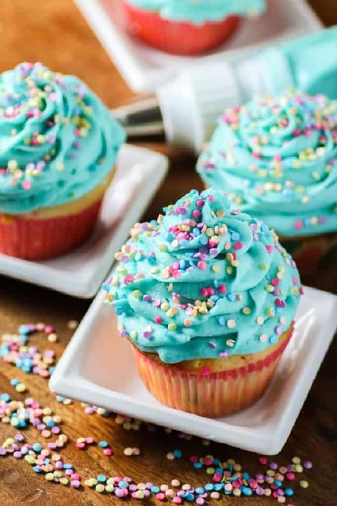 Birthday cupcakes with blue frosting and sprinkles on small white plates