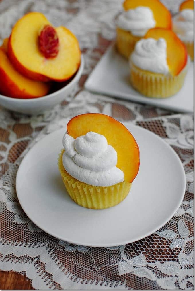 peaches N cream cupcakes on a white plate and a bowl of sliced peaches