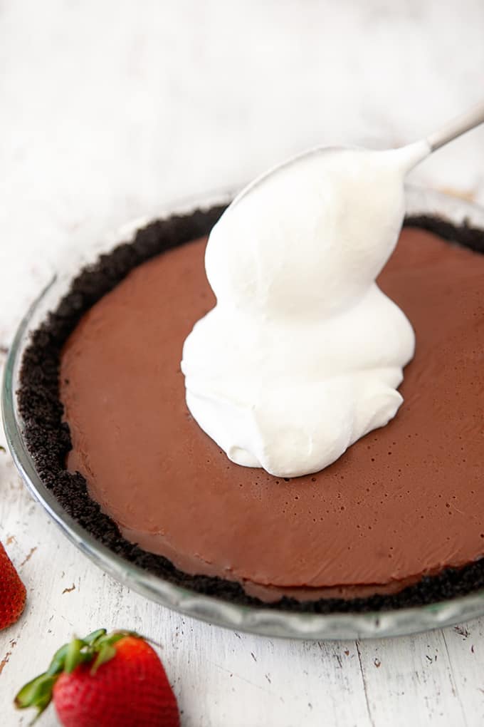 Putting whipped cream topping on a chocolate pudding pie