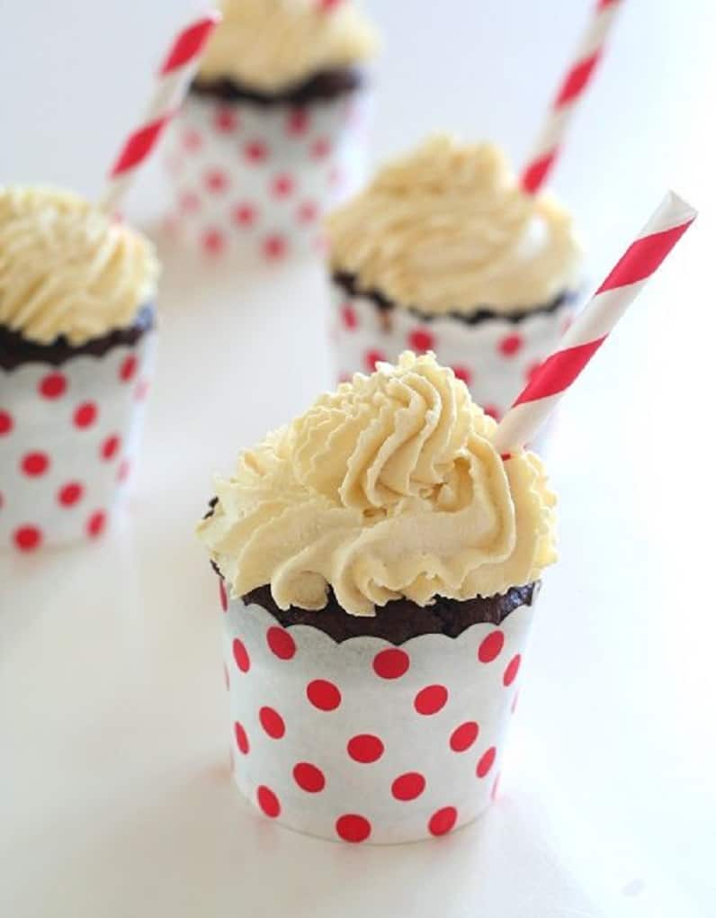 Root beer float cupcakes on a white table with a straw sticking out