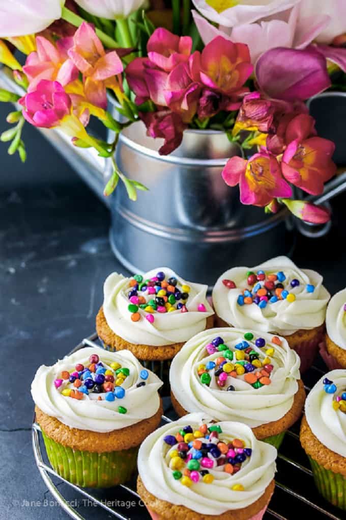 White chocolate coconut cupcakes whith sprinkles on a wire rack