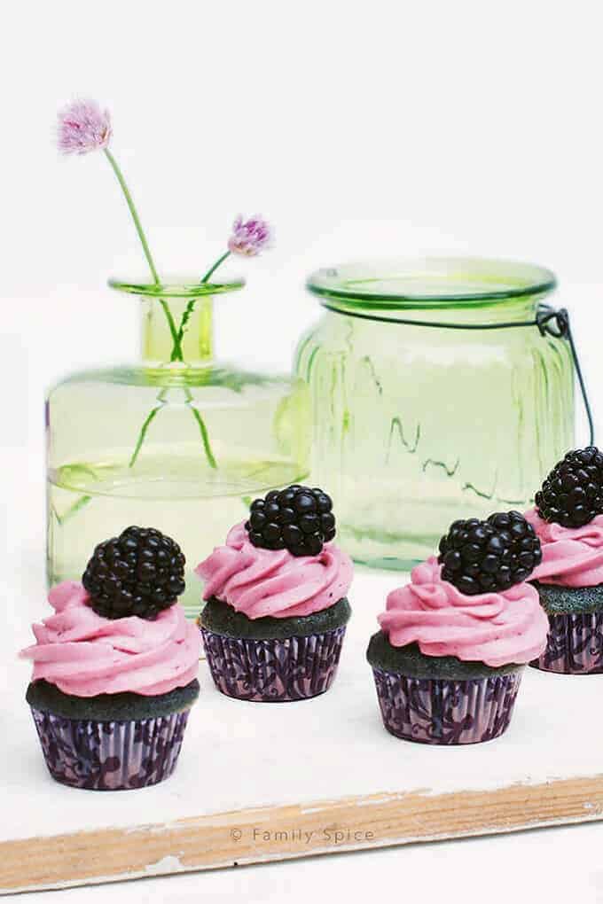 Blackberry and honey cupcakes on a white board with a green jar in the background