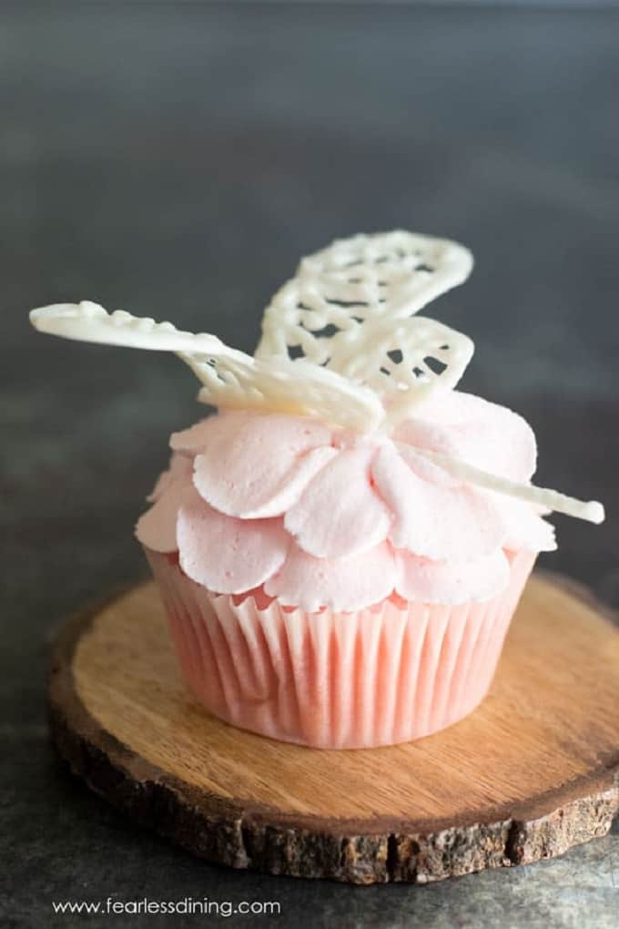 Pink Lemonade cupcake with a butterfly lace icing on top on a wooden board