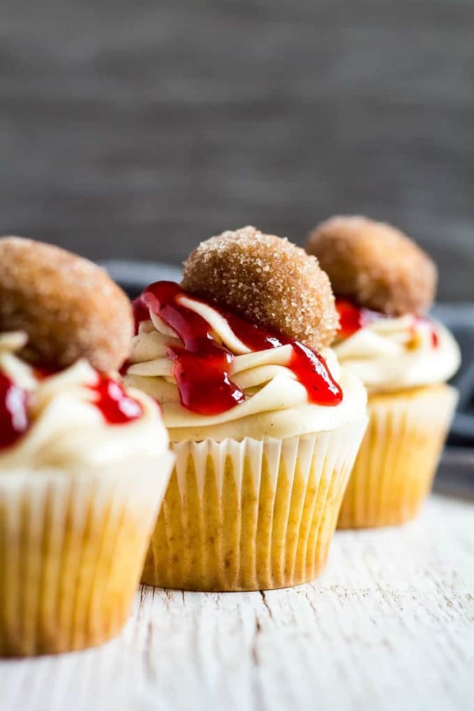 Jam donut cupcakes with strawberry jam, a small donut hole and white frosting on a white board