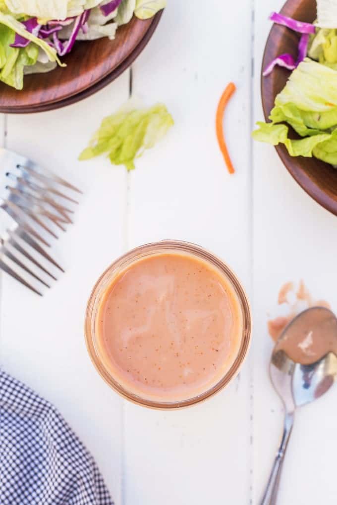 Overhead shot looking into a jar of salad dressing with bowls of salad at the top. 