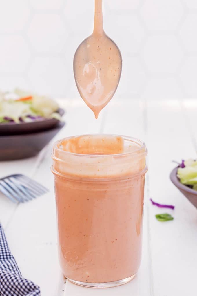 A spoon coming vertically out of a jar of salad dressing. 