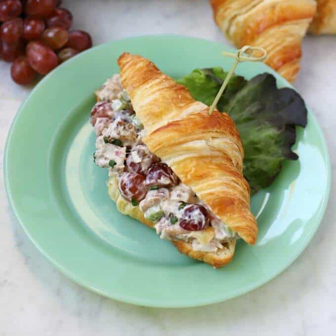 A green plate containing a croissant filled with chicken salad