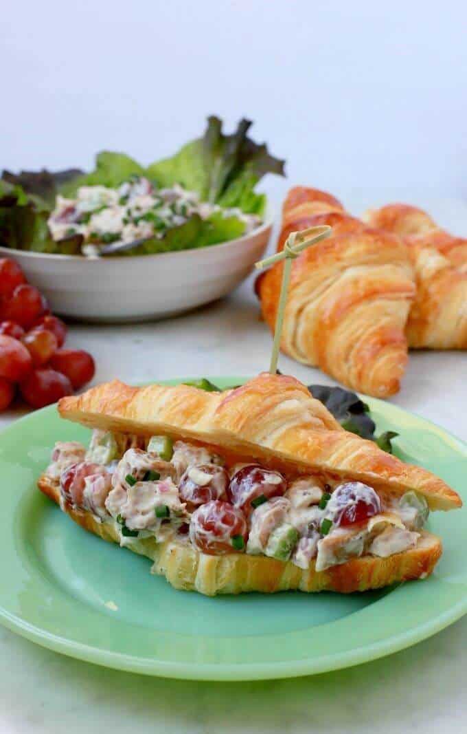 A green plate containing a croissant filled with chicken salad.