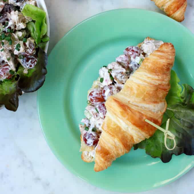 An overhead shot of a green plate containing a croissant filled with chicken salad