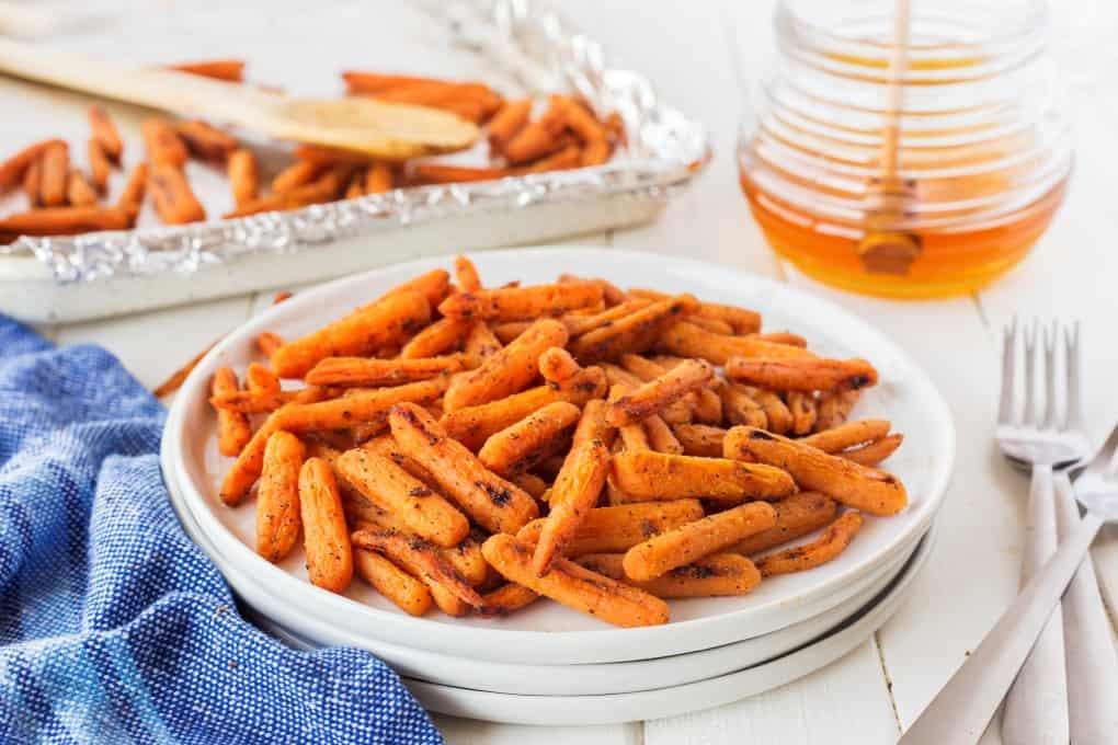 White plates of carrots with a pot of honey