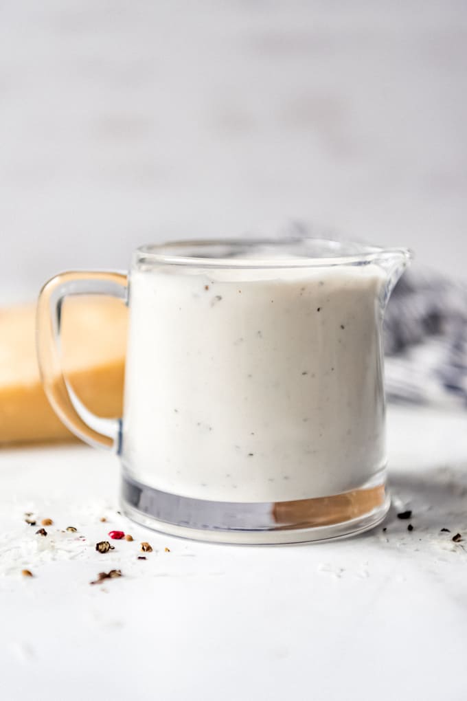 Parmesan peppercorn dressing - A glass pitcher filled with parmesan peppercorn dressing next to a wedge of parmesan cheese.