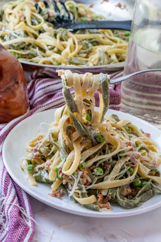 A twirl of Straw and Hay pasta on a fork from a plate of pasta