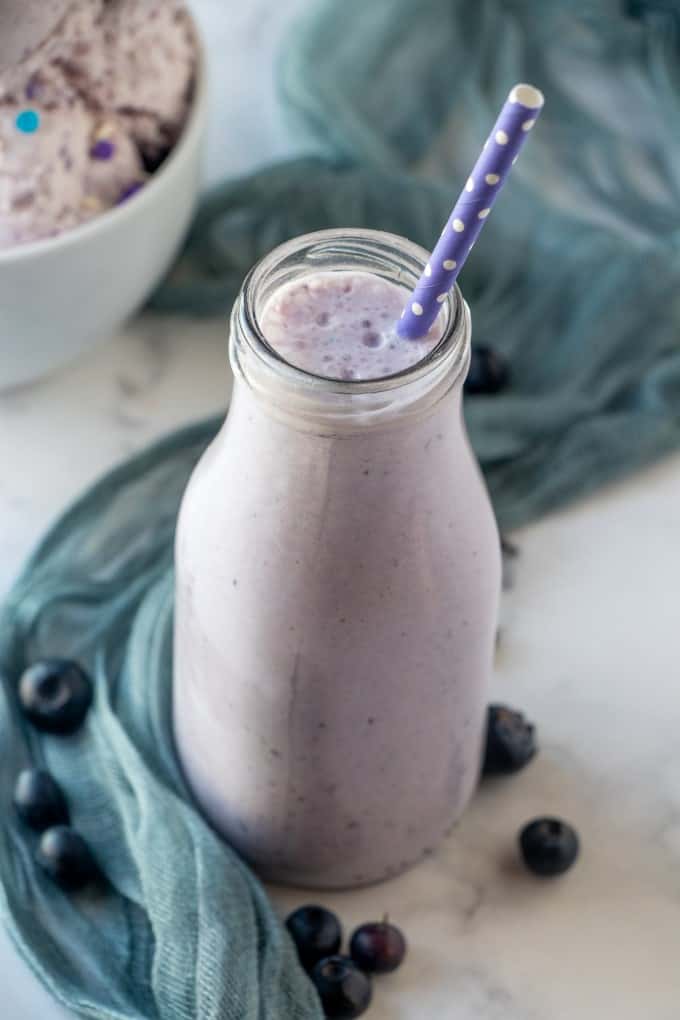 Blueberry milkshake in a glass bottle with a purple straw