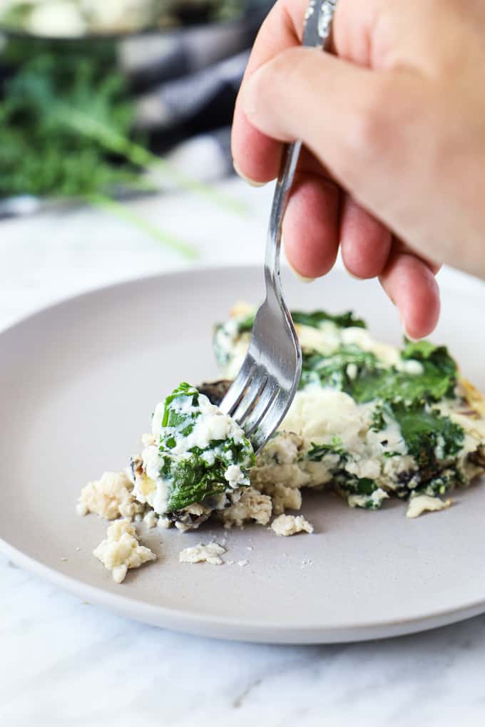 Close up of an egg white frittata in a beige plate with a hand holding a fork