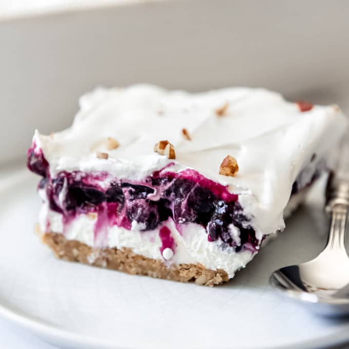 Blueberry Delight - a slice of layered no-bake blueberry cream cheese dessert on a plate with a spoon.