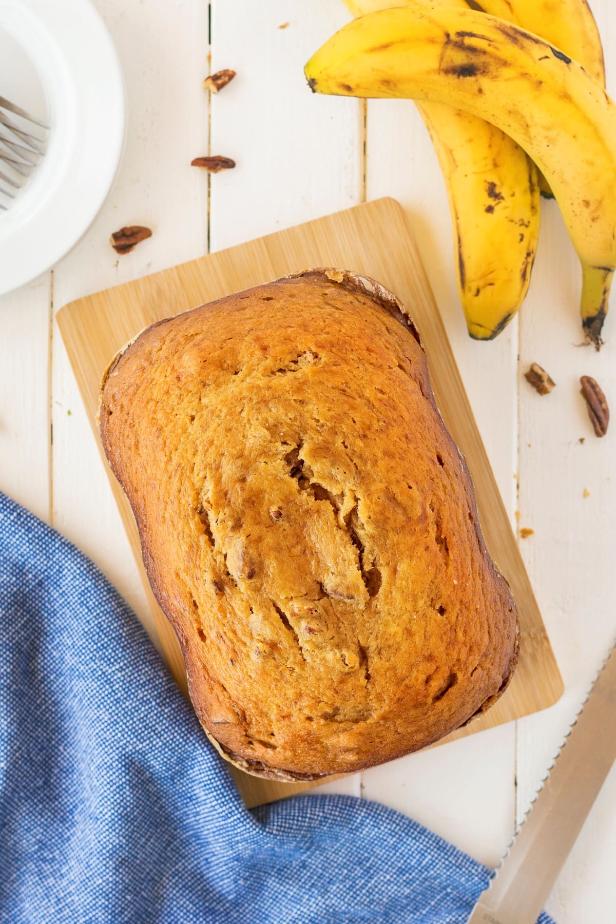 Overhead shot of a loaf of banana bread on a wooden bread board. 