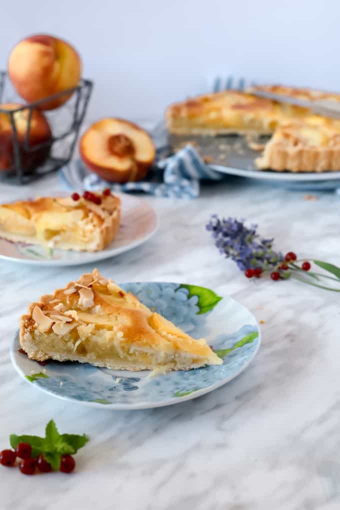 Peach Pie slice on a plate with peaches and pie in the background.