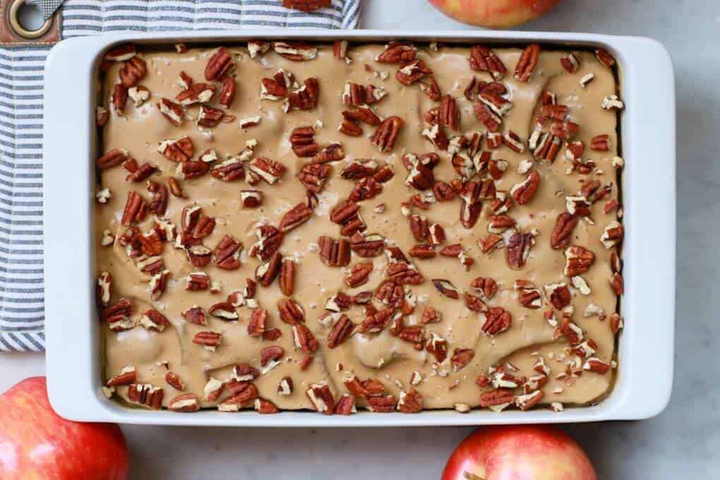 A white baking pan holds a golden baked Apple Dapple Cake topped with brown butter glaze and pecans.